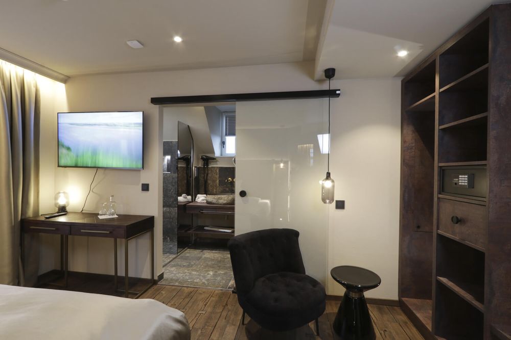 Nebst dem großen SmartTV liegt die gläserne Schiebetür die in das Badezimmer führt.