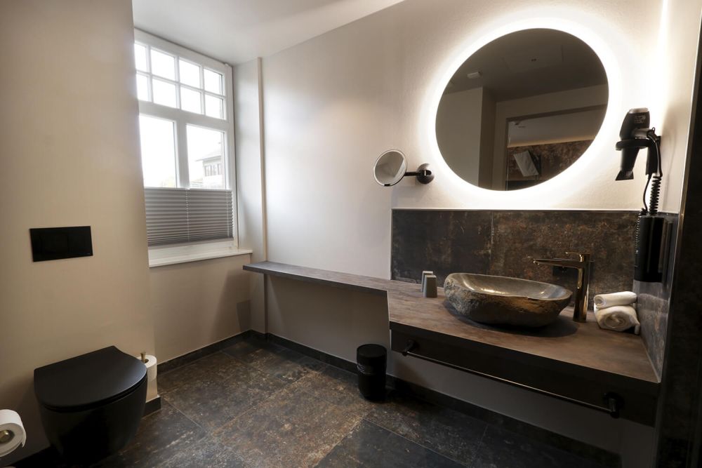 Das geräumige Badezimmer des Hotelzimmer 303 mit steinernem Waschbecken und indirekter Beleuchtung am Spiegel.